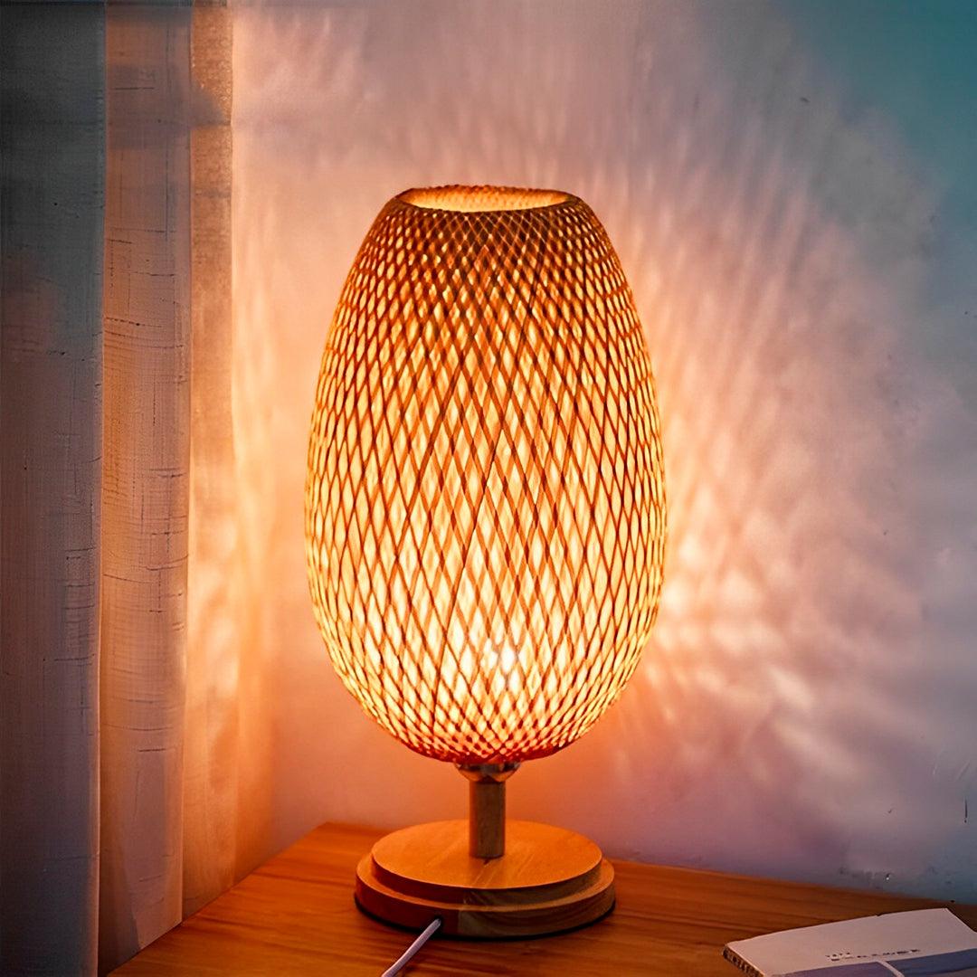Abajur de palha aceso no canto da mesa, projetando losangos de luz na parede