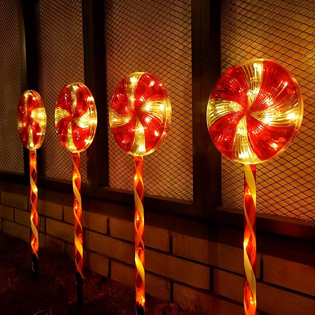 Pirulitos acesos em fila junto a um muro de tijolos e uma grade, à noite
