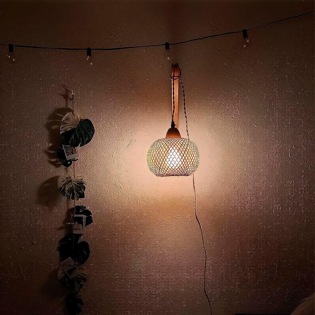 Esfera de bambu acesa numa parede escura, com luzes de varal e folhas ao lado