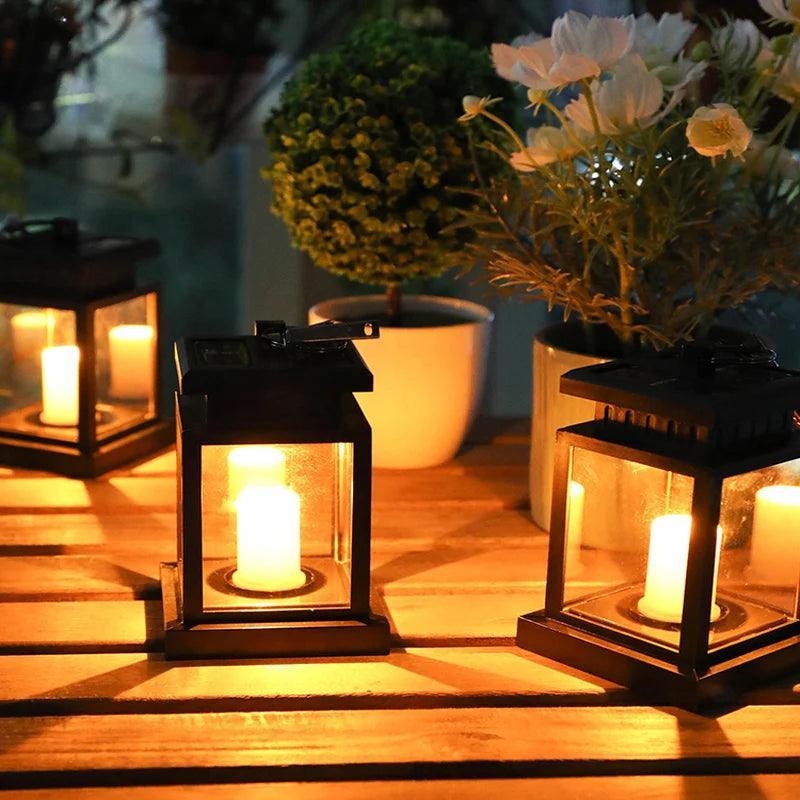 Lanternas acesas sobre mesa de madeira ao lado de vasos, com luz amarelada de vela